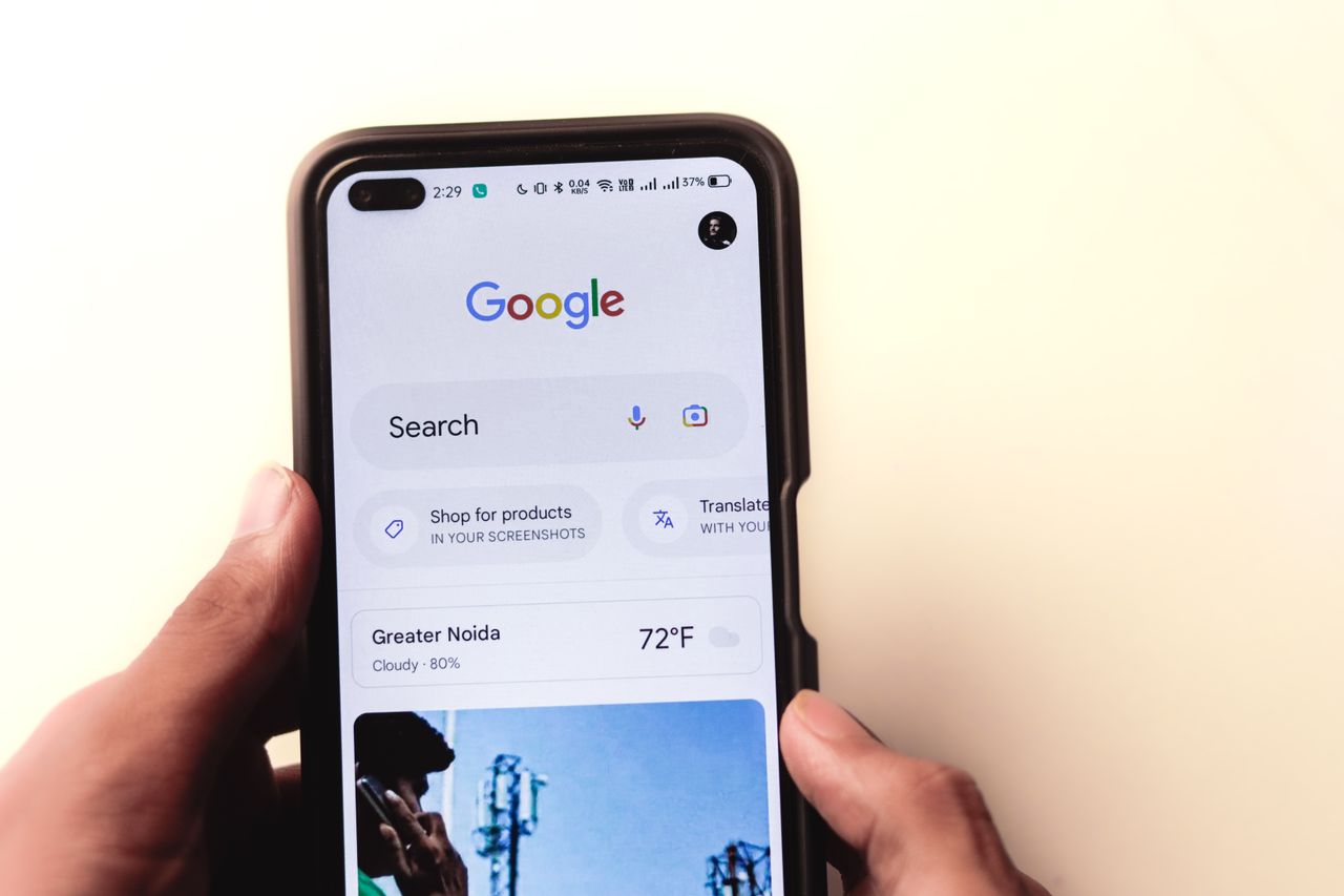 A tight close-up shows a hand holding a smartphone with Google search visible on the display.